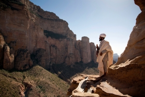 A priest stands on the edge of a cliff in front of the entrance to Ethiopian Orthodox rock-hewn church of Abuna Yemata Guh in the Gheralta Cluster in the Tigray mountains, on January 28, 2011, in Megab, Ethiopia.